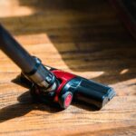 A high-angle view of a vacuum cleaner head working on a sunlit wooden floor.